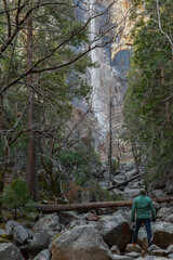 View of the winter Bridalveil Fall, trees, huge river rocks and Tuolumne River in Yosemite Park, California. A man makes his way to the waterfall through rocks and boulders.