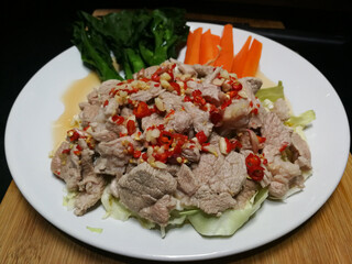 Pork with Lemon spicy-sweet sauce with chili and garlic mixed with sour lemon juice. Arrange the dish with kale and carrots on a white plate placed on a wooden chopping board.
