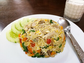 One kind of Thai breakfast Pork Fried Rice with Chicken Eggs With a mixture of carrots, kale, and tomatoes, decorating the edges of the dish by cucumbers On a white circular plate