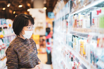 Beautiful Asian senior adult looking for cosmetic products at convenience mall during the Coronavirus, COVID19 outbreak. Social distancing and using protective face mask during the COVID-19 pandemic.
