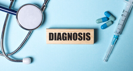 The word DIAGNOSIS is written on a wooden block on a blue background near a stethoscope, syringe and pills. Medical concept