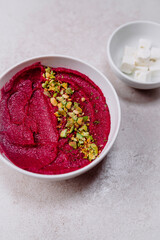 stock photography pink vegan and vegetarian beetroot hummus with pistachio in white bowl accompanied by feta cheese and gray background