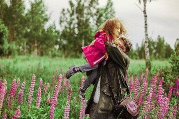 Father holds the dauther on his hands in the midst of lupin flowers.