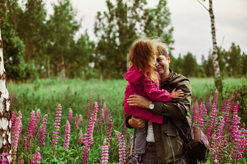 Father holds the dauther on his hands in the midst of lupin flowers.