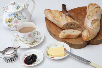 baguette, a cup of tea, butter, jam on a white table