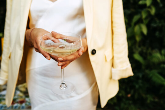 Woman dressed in white cocktail dress holding a coupe of champagne.