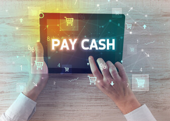 Close-up of a hand holding tablet with PAY CASH inscription, online shopping concept