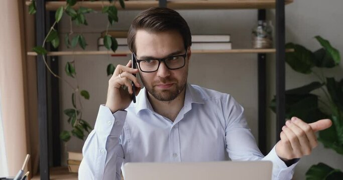 Businessman sit at workplace desk in front of laptop holding smartphone talking with client gesticulating having lively positive conversation explain provide support help to customer distantly concept