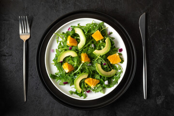 Salad with avocado, orange, ruccola and red onion on black stone background.  Horizontal orientation.  Flat lay. 