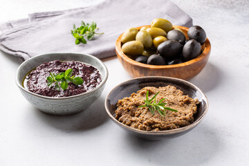 Tapenade - paste made from olives. Bowls with spreadable black and green olive cream on concrete background.
