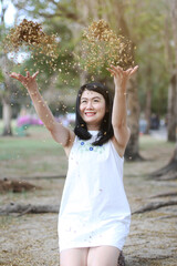 Beautiful asian woman in white dress relax and smiling with Sprinkle leaves in nature park. Thai girl or Chinese Girl enjoy on holiday in the Garden