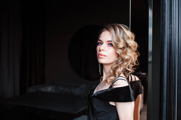 Beautiful blonde, young girl. Portrait of a young girl in a restaurant. Young girl in a restaurant on a black background. Portrait of a girl in a black dress. Young girl.
