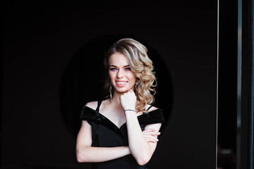 Beautiful blonde, young girl. Portrait of a young girl in a restaurant. Young girl in a restaurant on a black background. Portrait of a girl in a black dress. Young girl.