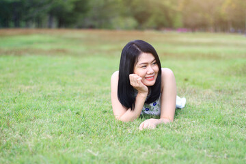 Beautiful asian woman in white dress relax and smiling on green field in natural park. Young Thai girl enjoy on holiday with sunlight in garden