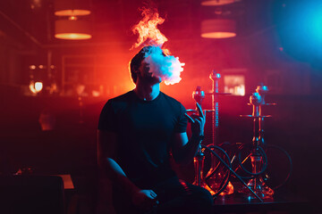 young guy smokes a shisha and lets out a cloud of smoke