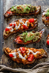 Baked sweet potato toasts with roasted chickpeas, tomatoes, goat cheese, sauce guacamole, avocado, seedlings on baking tray over brown background. Healthy vegan food, clean eating, top view