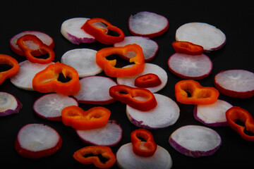 A variety of colorful and chopped red and yellow vegetables and fruits with a black background.