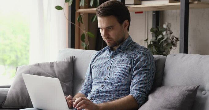 Guy sit on sofa put pc on lap texting received acceptance e-mail bank loan approval notice feels excited clenched fists makes yes gesture. Lucky moment, sincere emotion victory result achieve concept