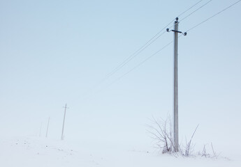 Electric poles in winter . Snowy Landscape with fog in the Morning