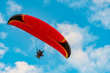 Red dome of a motor paraglider flying on a background of blue cloudy summer sky. Tandem on a...