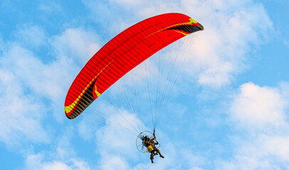 Red dome of a motor paraglider flying on a background of blue cloudy summer sky. Tandem on a paraglider high in the sky.