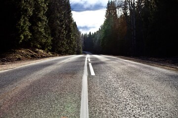 Obraz premium Straight empty asphalt road through the coniferous forest. Modern countryside road leading into the distance. Highway surface close up. Diminishing perspective road view. Traveling by car. Road trip.