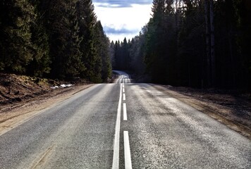 Straight empty asphalt road through the coniferous forest. Modern countryside road leading into the distance. Highway surface close up. Diminishing perspective road view. Traveling by car. Road trip.