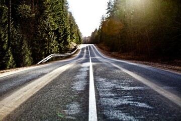 Fototapeta premium Straight empty asphalt road through the coniferous forest. Modern countryside road leading into the distance. Highway surface close up. Diminishing perspective road view. Traveling by car. Road trip.