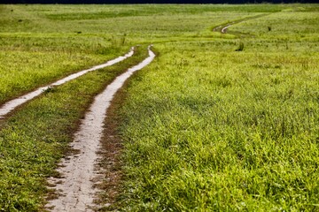 Dirt countryside road leading into the distance through the fields. Countryside roads. Perspective road view. Traveling by car. Car ride on a dirt road running through the field. Off road trip.