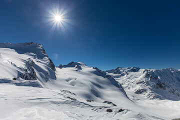 Sunny snowy day in Alps. Snow-covered white mountain peaks. Bright blinding sun. Blue sky. Winter Mountains landscape. Highlands nature. Nature Backgrounds. Snowy mountain range.