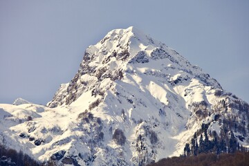 Snowcapped mountain peak among the clouds. Snowy mountains winter landscape on cloudy sky background. Winter snowy day in mountains. Snow-covered white mountain top. Snowy mountain range.