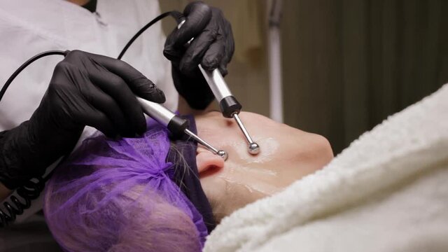 The beautician performs the microcurrent procedure in the beauty salon. The procedure stimulates collagen production, lifting, fights wrinkles, facial muscle tone, lymphatic drainage.