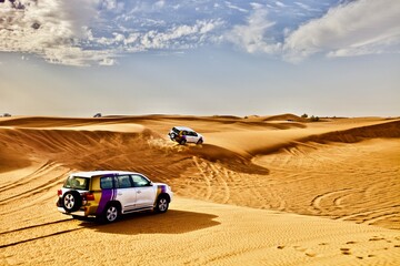 Fototapeta na wymiar Off road cars riding fast on dunes slopes in the desert in hot sunny day. Car safari among sand dunes in the desert. Traveling by car in the desert. 4x4 cars. Off road trip. Desert off-road racing.