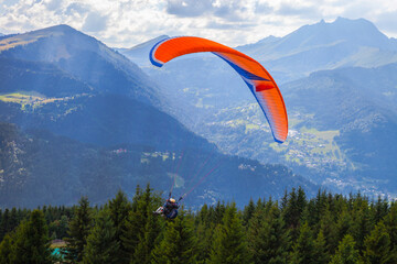 Paragliding high among the mountains in sunny summer day. Extreme Sports in the Mountains. Paraglider flight on mountains and bright sunny sky background. People Flying high in the sky. Freedom