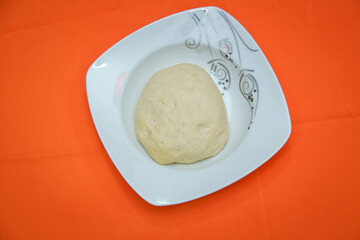Fototapeta na wymiar Raw dough lying on the plate on a white background. A piece of dough for bread baking . The dough is on a white plate on an orange background .