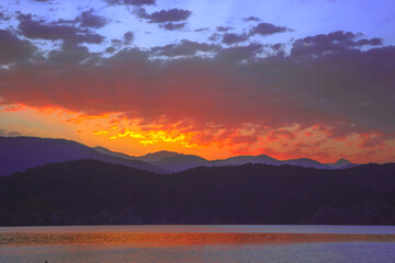 Sunrize yellow, red, orange light splash on morning sky, mountain and sea view, clouds shaped by colors