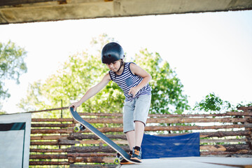 Skater boy rides on skateboard at skate park ramp. Kid practising skateboarding outdoors on skatepark. Youth culture of leisure and sports. Skateboarder doing trick on skateboard on halfpipe ramp