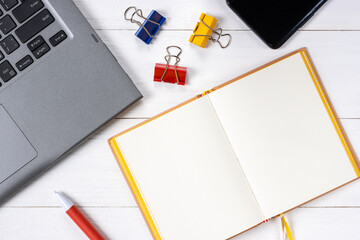 Laptop cellphone paper clips and notepad on white wooden background
