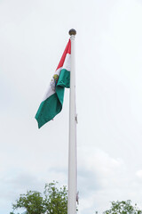 Flag of Hungary on the mast waving in the wind with cloudy sky background. Europe Hungary