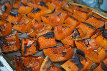 Traditional autumn dishes from pumpkins. Roasted pumpkin slices on a tray. Background of old gas furnace and mud wall.
