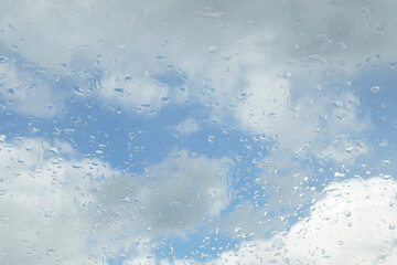 Raindrops on the window glass. Clear blue sky with white clouds. Blurred background.