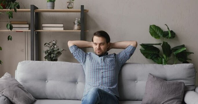 Serene man resting on couch puts hands behind head closed eyes enjoy fresh humidifier conditioned air. Male look into distance feels relaxed. New rented flat, homeowner, modern apartment owner concept