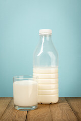 A bottle of milk and glass of milk on a wooden table, blue background