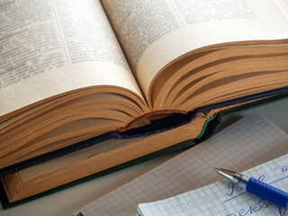 Old thick books are open and lie on the table. Notebooks and a pen are visible nearby. The concept of education, scientific work, independent study of literature.