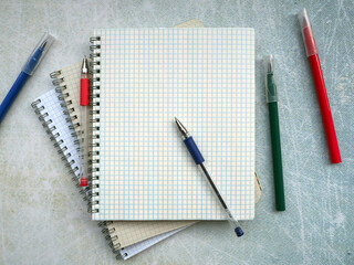 Open notebooks are fan-folded on top of each other. On top are the pens. Nearby are colored markers. You can write text on a blank sheet. Education concept