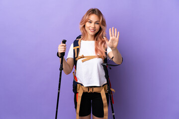 Teenager girl with backpack and trekking poles over isolated purple background counting five with fingers