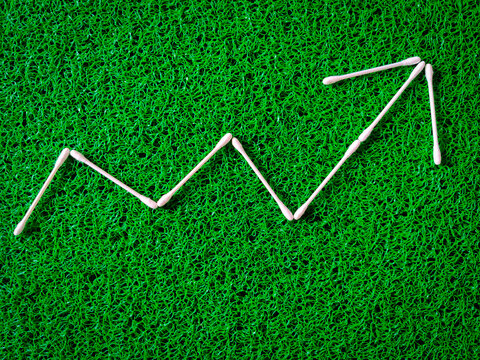 Cotton ear sticks arranged as a Increase and decrease graph on green background. Business concept