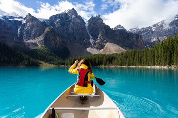 Girl kayaking on a turquoise lake with a yellow rain jacket in summer
