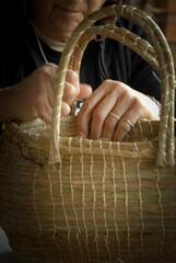 craftsman's hands sewing with thread a basket of vegetable fiber