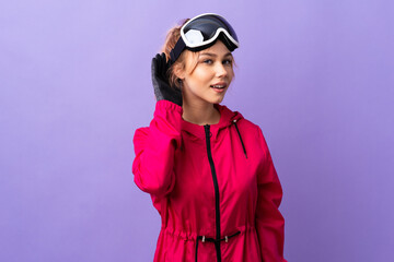 Skier teenager girl with snowboarding glasses over isolated purple background listening to something by putting hand on the ear